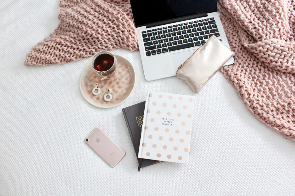 Image of Laptop, journal, and phone sprawled on a blanket across a white bed