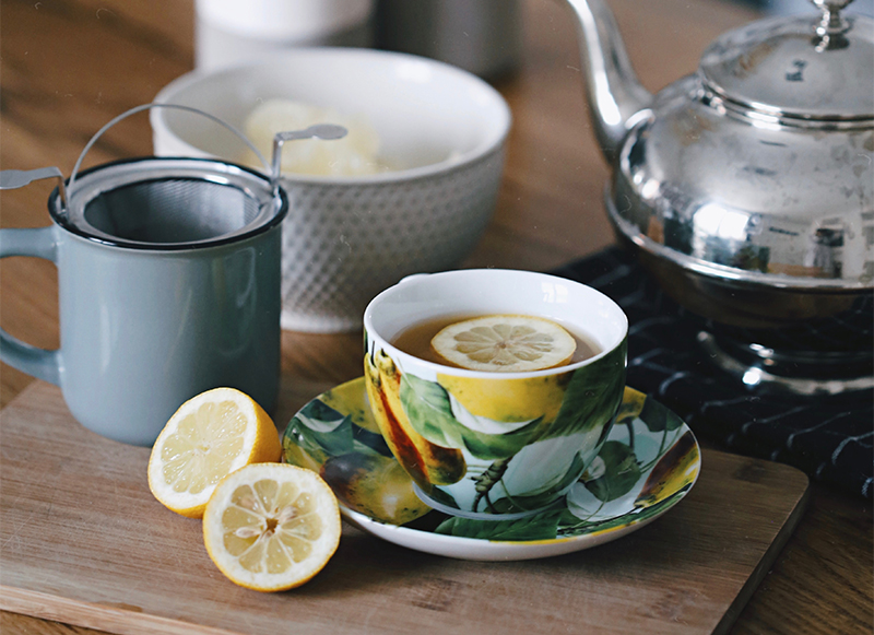 Image of hot tea with lemons, a tea kettle, and cup with tea infuser 